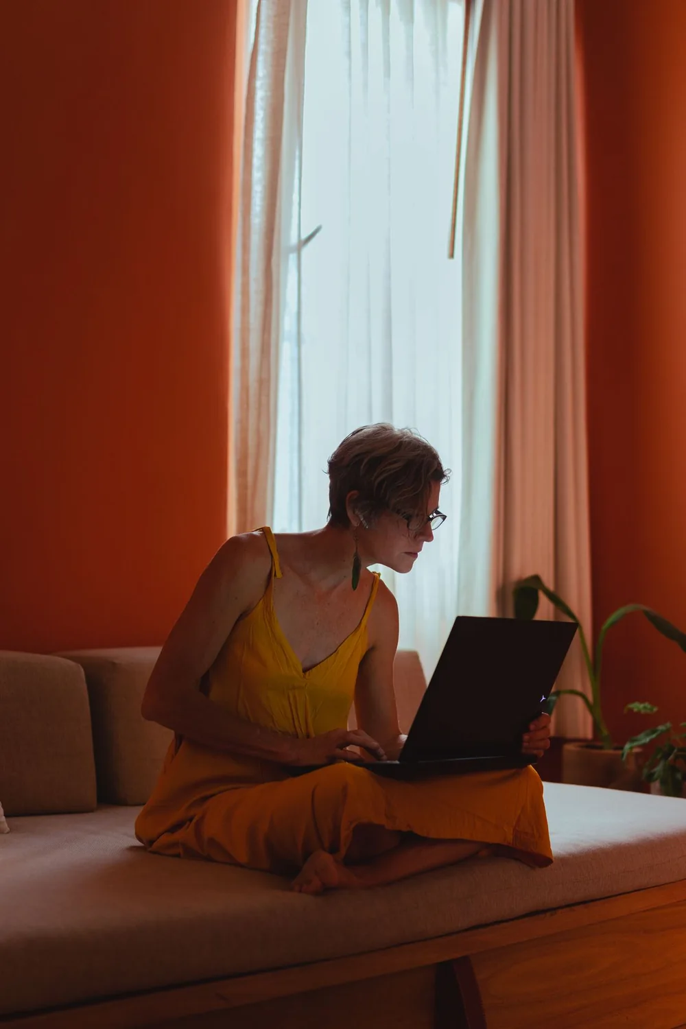 Femme utilisant son ordinateur portable à la maison, assise sur un canapé