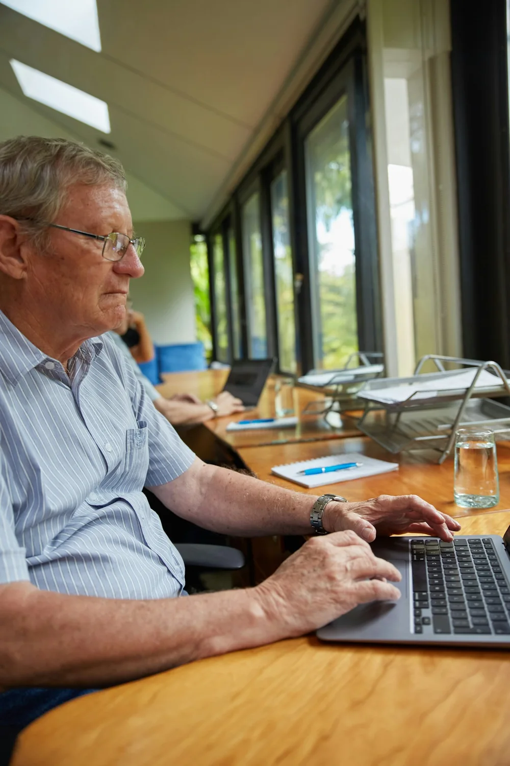 Homme utilisant un ordinateur portable à une table près de grandes fenêtres