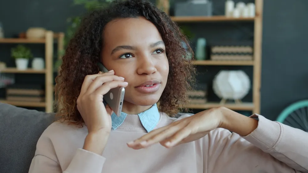 Femme en conversation téléphonique, assise sur un canapé chez elle