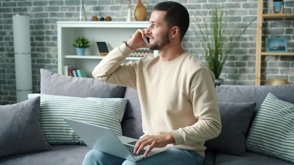 Homme au téléphone, un ordinateur portable sur les genoux dans un salon
